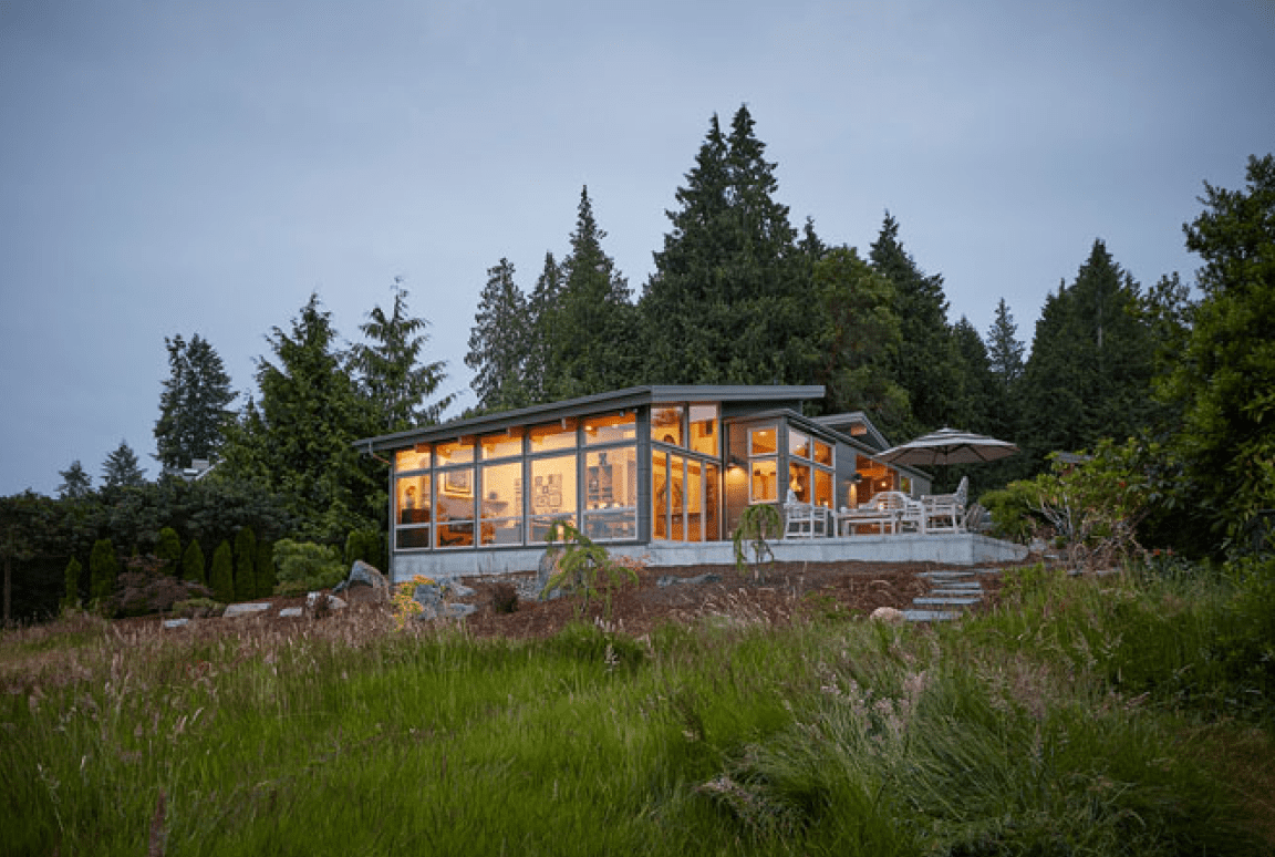 Frame 2095584753 Modern glass house surrounded by lush greenery.